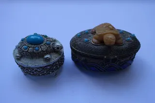 Das Döschen aus Florenz steht auf kleinen Füßen und ist mit Halbedelsteinen besetzt, Größe 4,5 cm. Die filigrane Metallarbeit rechts ist u.a. teilemailliert, mit Schnappverschluß, Größe 6 cm.