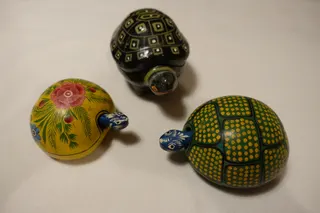 Zwei handbemalte Kalebassen mit Wackelkopf aus Mexiko und eine Dose (oben) aus Pappmaché, innen schwarz lackiert, aus Kaschmir (Indien).
