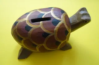 Spardose, ausgehöhlt und bemalt, mit Schieber im Boden zu öffnen, Größe 17 cm. Mit Münzen gefüllt dient sie auch als Rassel.