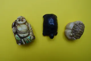 Netsuke, zeitgenössisch nachempfunden, aus verschiedenen Ländern und div. Materialien; links: die Schildkröte scheint der buddhaähnlichen Gestalt erfreuliches ins große Ohrwaschel zu flüstern.