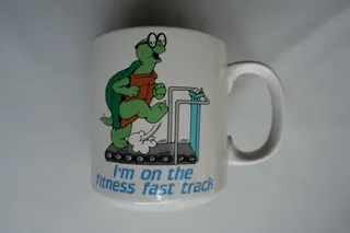 Becher der Firma Russ Berrie, Oakland, USA, Made in Korea, mit rückseitigem Text "Certified Fitness Freak". Wer hätte gedacht, dass sich selbst Schildkröten fit halten müssen?