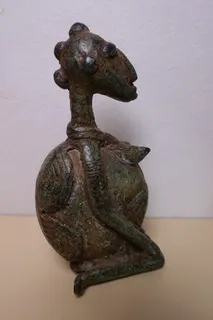 Kupferguß der Dogon, Höhe 10 cm. Die hockende Frau mit stilisierter "Haarpracht" wirkt schwanger, hält mit der linken Hand ein Kind (hier nicht zu sehen) und trägt an Bauch und Rücken eine Art Panzer.