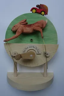 Mechanische Holzskulptur aus Essex (Großbritannien), handbemalt, sign., Höhe 28 cm. Mittels einer Kurbel und 5 rückseitigen Zahnrädern überholt die im Auto sitzende Schildkröte den elegant rennenden Hasen beliebig oft (in freier Anlehnung an die Fabel von Aesop und La Fontaine). Es gibt noch eine zweite, bewegbare Skulptur von ihm. Ein dankenswerter Kontakt ergab sich - wie bei einer ganzen Reihe weiterer Künstler - über Elke Hügel, Galerie Handwerk, München.