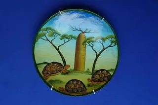 Schale (Durchmesser 20 cm), handbemalt mit den nur noch seltenen Sternschildkröten und einem Affenbrotbaum (Baobab). Der mittige Baum ist das Wahrzeichen der Insel Madagaskar, wird 800 Jahre alt und gehört zu den Naturwundern der Welt. Die Früchte sind Nahrungsmittel und dienen der Volksmedizin.