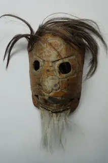 Maske auf der Basis eines Schildkrötenpanzers, Augen, Mund und Nasenlöcher wurden ausgeschnitten und das Schildpatt beschnitzt, um das Gesicht heraus zu arbeiten, das Tierhaar ist auf Lederstreifen aufgenäht. Das Objekt stammt aus Afrika, genauer aus Deutsch-Ostafrika, der größten Kolonie des Deutschen Reiches (es umfasste die heutigen Länder Tansania, Burundi und Ruanda), um 1900, Größe 30 cm.