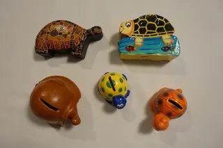 Die Spardosen aus Leder, mit einem Druckknopf zu öffnen (links), Pappmaschee (rechts) und Keramik (unten) kommen aus diversen Ländern. Das umgangssprachliche Wort "Kröten" steht für Münzen/Kleingeld (siehe auch Redewendung: "rück deine Kröten raus").