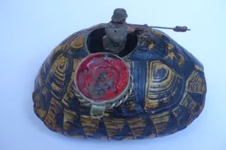 Kompletter Panzer einer Griechischen Landschildkröte (Testudo boettgeri), mit schön ausgeprägtem Muster, in der Bodenplatte ist deutlich ein Schmetterling (s. eigene Seite, bzw. "Suche : Schmetterling") wahrnehmbar, Größe 17 cm. Oben wurde ein metallgefasster Deckel mit Scharnier eingelassen. Klappt man diesen auf, ist ein eingebautes Metallgefäß für Siegellack zu sehen, Tiefe 4 cm. Erworben im Antikpalast (München), eine englische Arbeit um 1890. Durch den schlichten Eingriff mit einem Spielzeug-Soldaten (vom Flohmarkt) wird die doppelte Bedeutung des "Panzers" hervorgehoben.